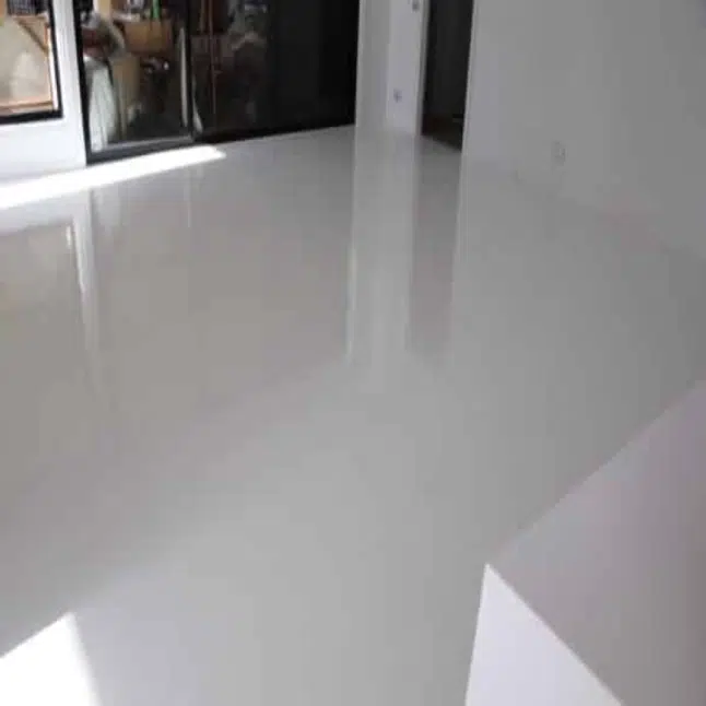 A bright minimal room with glossy white flooring reflecting the light from large windows and a sliding glass door