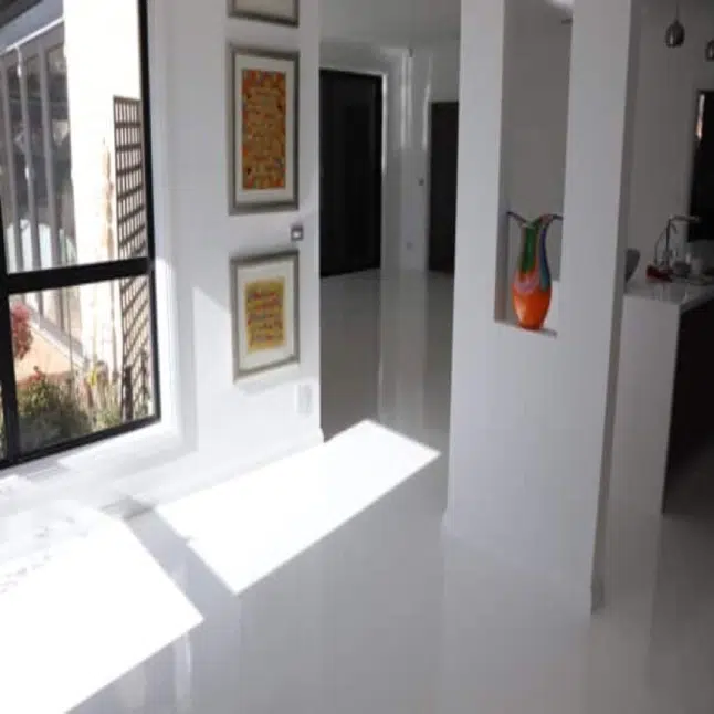 Bright modern interior with glossy white floors wall art and sunlight streaming through large windows