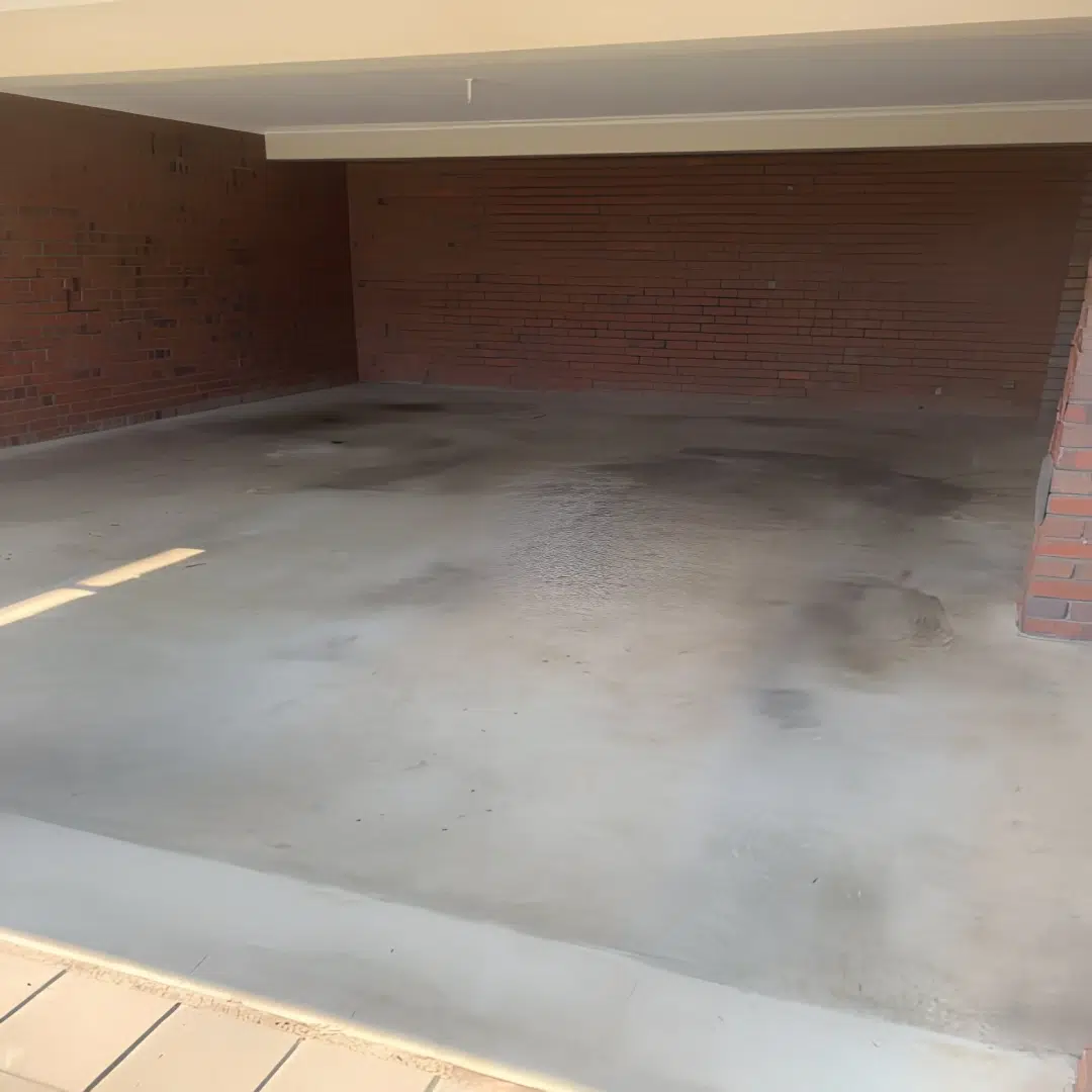 Freshly coated epoxy garage floor next to a brick wall and paver driveway