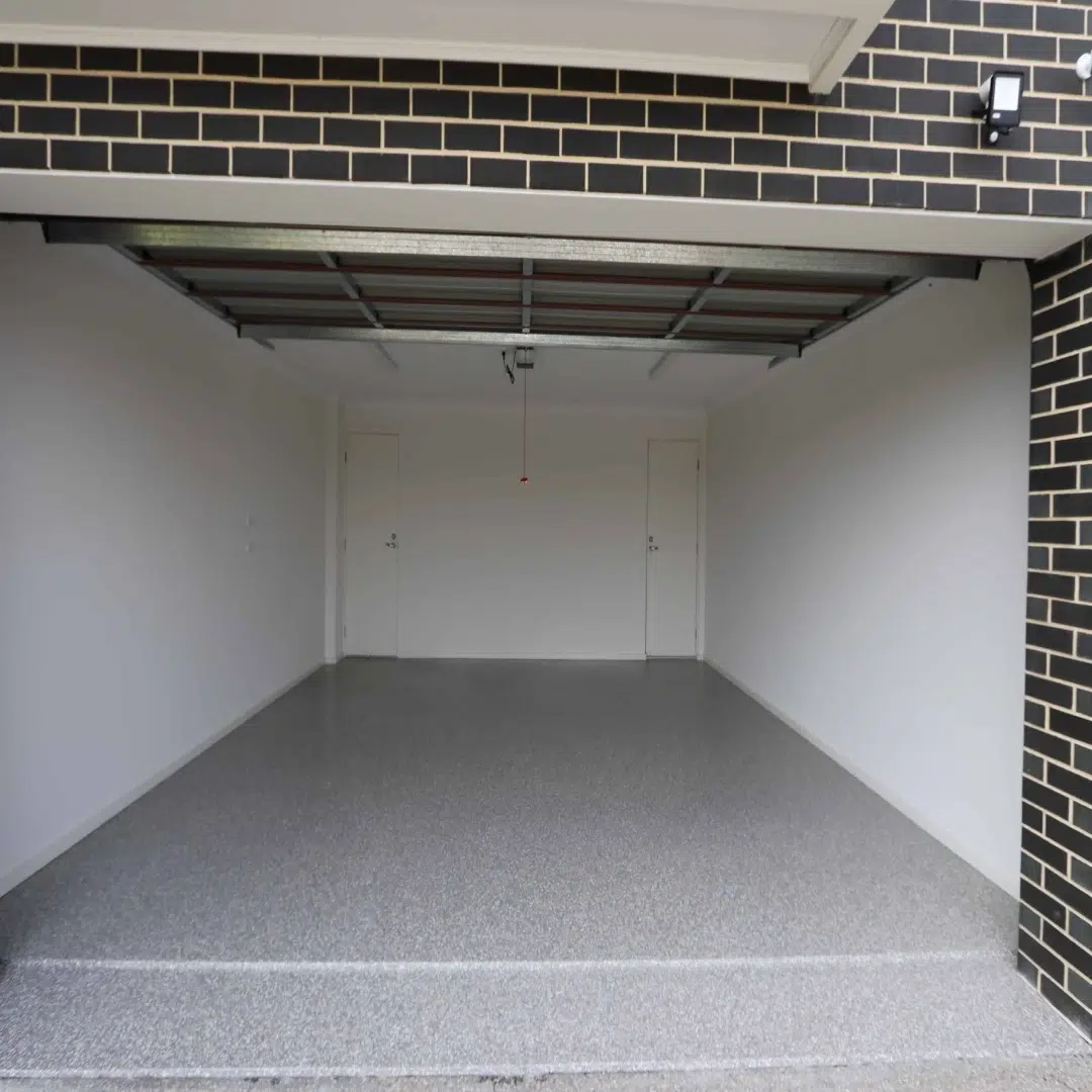 Open empty two car garage with a clean epoxy floor and two white doors at the back